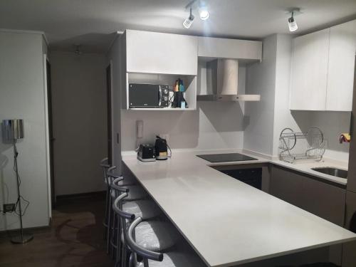 a kitchen with a white counter and chairs in it at Departamento en Papudo in Papudo