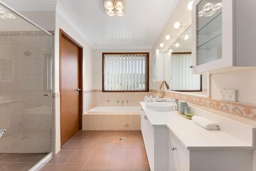 a white bathroom with a tub and a sink at Shell Cove Coastal Haven in Shellharbour