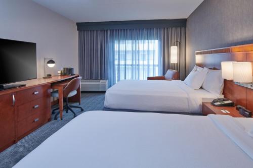 a hotel room with two beds and a desk and a television at Courtyard by Marriott Detroit Livonia in Livonia