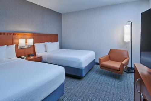 a hotel room with two beds and a chair at Courtyard by Marriott Detroit Livonia in Livonia
