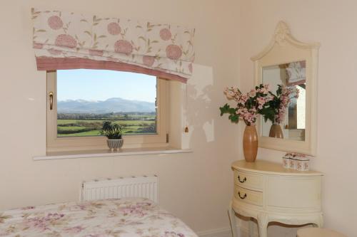 a bedroom with a window and a dresser with a vase of flowers at Cosy Barn in Dwyran