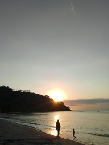 a woman and child walking on the beach at sunset at MBE BALENG KU in Mangsit