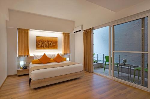 Nest By Rivido Apart Hotel, Bannerghatta road في بانغالور: غرفة نوم مع سرير مع وسائد برتقالية وشرفة