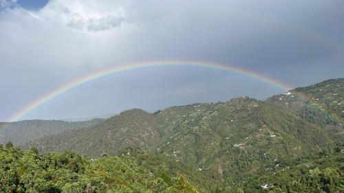 a rainbow in the sky over a mountain range at EcoEscape Mukteshwar in Mukteswar
