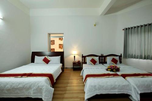 two beds in a room with white walls and wooden floors at Nhà Nghỉ Hoàng Yến Phan Rang in Kinh Dinh