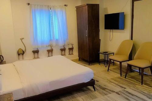 a bedroom with a bed and two chairs and a television at Valley Nest for 6-12 PAX in Mount Ābu