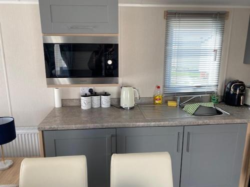 a kitchen with a counter with chairs and a sink at Duffy's Den - Parkdean California Cliffs - Fulmar 45 in Scratby