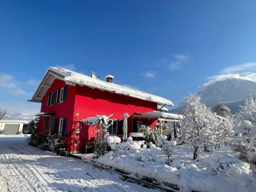 a red house covered in snow with a mountain in the background at Ferienwohnung Seidenhuhn in Kiefersfelden