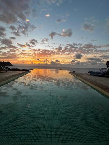 una piscina en la playa con una puesta de sol en el fondo en Palmeira Da Cruz EcoLodge en Chã da Igreja