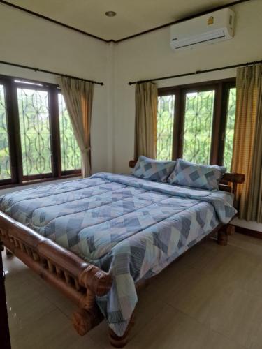 a bedroom with a bed with a blue comforter and windows at Bungalow vue mer in Amphoe Koksamui