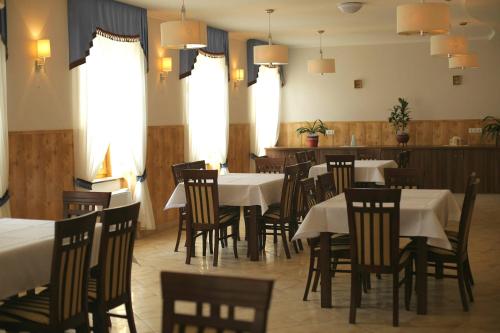 a dining room with white tables and chairs and windows at Meggyes Hotel in Szerencs