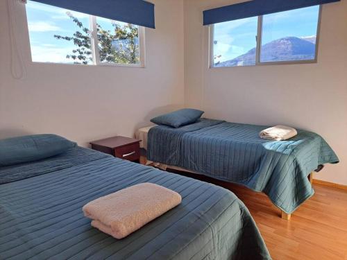 two beds in a room with two windows at Cómodo departamento full equipado en Coyhaique in Coihaique