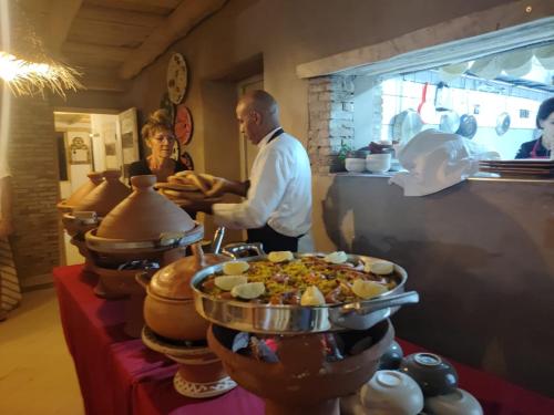a couple of people standing in a kitchen with food at Hôte sahara & spa TADIGHOUST in El Hara