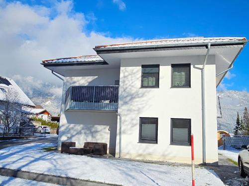 une maison blanche dans la neige avec des montagnes en arrière-plan dans l'établissement Ferienwohnung in Arnoldstein, à Arnoldstein