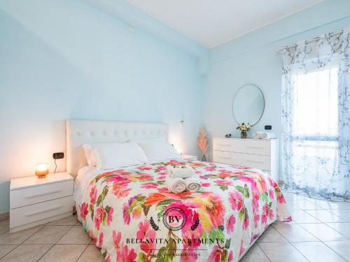 a white bedroom with a bed with a floral bedspread at BellaVita Apartments in Assemini