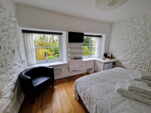 a bedroom with a bed and a chair and two windows at Primrose Cottage in Helston