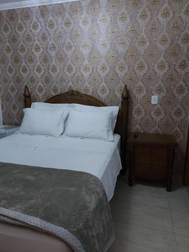 a bed with white pillows and a night stand in a bedroom at Casa Amarela Pousada in Domingos Martins