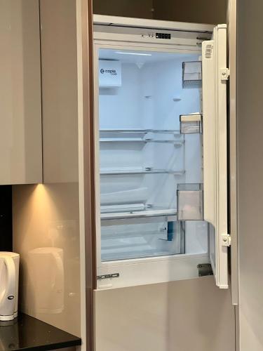 an empty refrigerator with its door open in a kitchen at Kensington House by MNK Estates in Slough