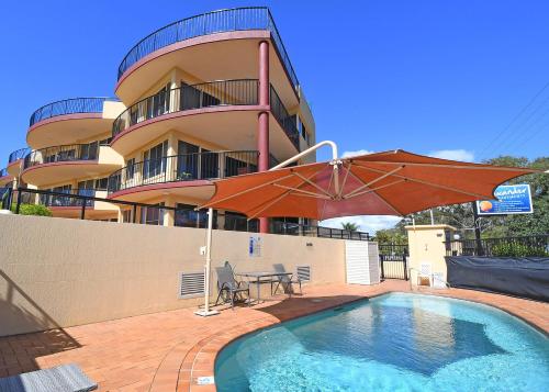 a swimming pool with an umbrella and a building at Alexander Beachfront Apartments in Hervey Bay