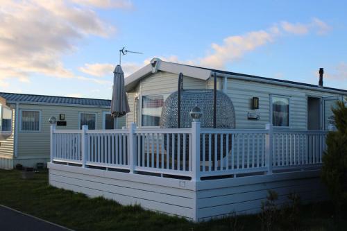 uma casa móvel com uma cerca branca e um guarda-chuva em Cosy beachfront getaway in Mersea em West Mersea