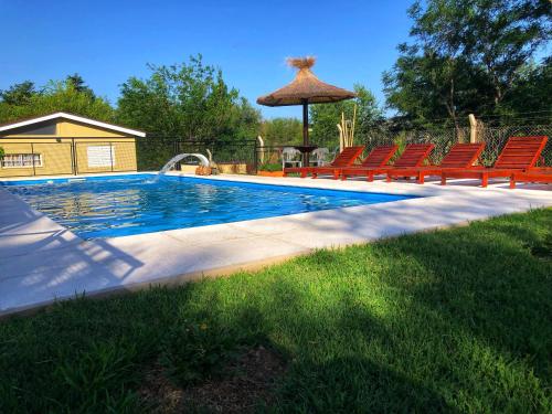 a swimming pool with red chairs and an umbrella at Monoambiente in San Antonio de Arredondo