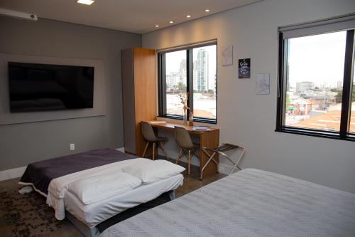 1 dormitorio con 2 camas, escritorio y ventanas en Flat Tatuapé Sua Casa Your Home en São Paulo