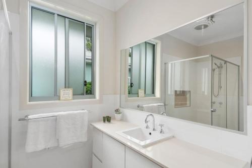 een witte badkamer met een wastafel en een spiegel bij Coastal Palms Escape - Your Ideal Family Getaway in Barrack Point