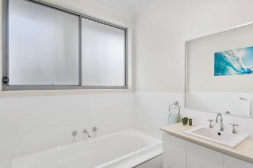 a white bathroom with a tub and a sink at Coastal Palms Escape - Your Ideal Family Getaway in Shellharbour