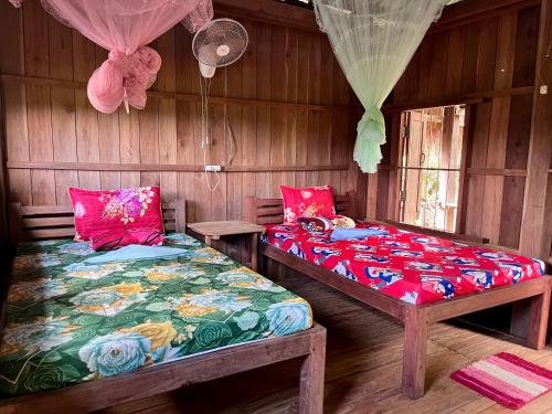 two twin beds in a room with wooden walls at Ratanakiri Farmhouse & Trekking in Banlung