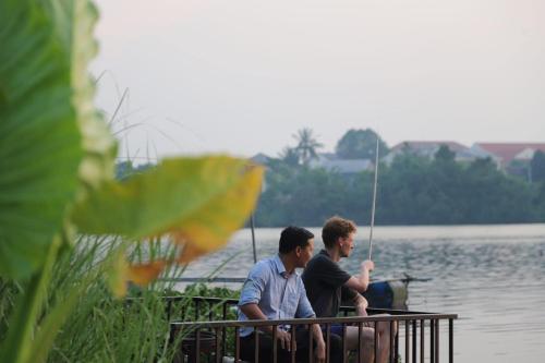 two men sitting on a dock in the water at La Y Riverview in Hue