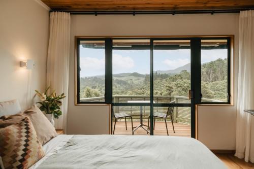 a bedroom with a large window and a table and chairs at Buffalo Lodge in Coromandel Town