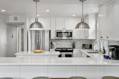 a white kitchen with white cabinets and stainless steel appliances at Stunning Beach Home with Fireplace, Fast WiFi, Grill & Outdoor Seating! in San Diego