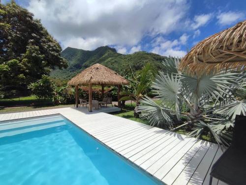 a swimming pool with a straw umbrella and a resort at Charmante villa de vacances à Moorea in Afareaitu
