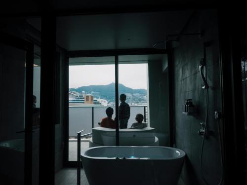 FAV LUX Nagasaki في ناغاساكي: حمام مع حوض استحمام و شخصين كانا ينظران من النافذة
