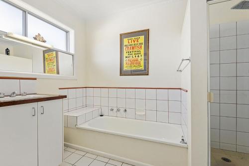 ein weißes Bad mit einer Badewanne und einem Fenster in der Unterkunft Golden Bouy in Point Lonsdale