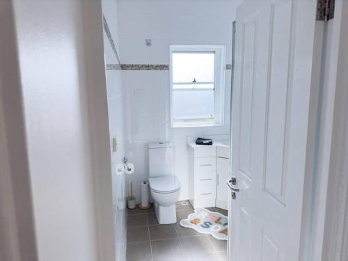 een witte badkamer met een toilet en een raam bij On The Esplanade - Close to beach & Cronulla mall with Aircon in Cronulla