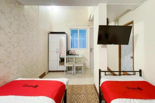 2 Betten in einem Zimmer mit einem TV und einem Schreibtisch in der Unterkunft RedDoorz Syariah at Prapen Jaya Surabaya in Surabaya