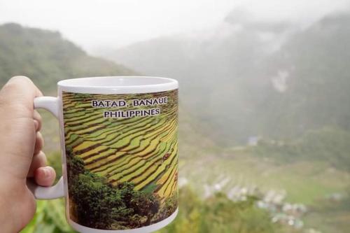 a person holding a coffee cup with a picture of a field at Batad Viewpoints Guesthouse and Restaurants in Banaue