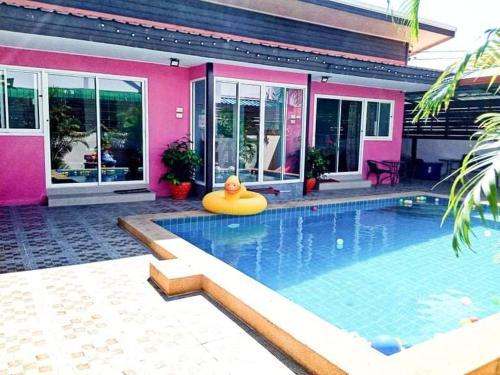 a swimming pool in front of a pink house at นาวินพลูวิลล่า in Bang Sare