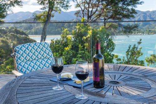 a bottle of wine sitting on a wooden table with two glasses at Tokongawa Retreat in Kaiteriteri