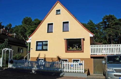 ein gelbes Haus mit einem weißen Zaun und einem Van in der Unterkunft Ferienwohnung zur Baaber Heide in Baabe