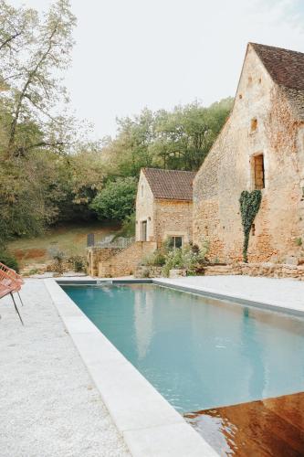 une piscine devant un bâtiment en briques dans l'établissement MAISON CISTUS - Maison d'hôtes de charme - Suites et gîte avec terrasses privées - Proche de Sarlat, au coeur de la Nature, à Sarlat-la-Canéda