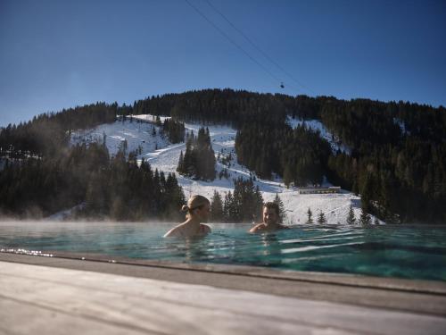 two people in a swimming pool with a snow covered mountain at Sporthotel Wagrain in Wagrain