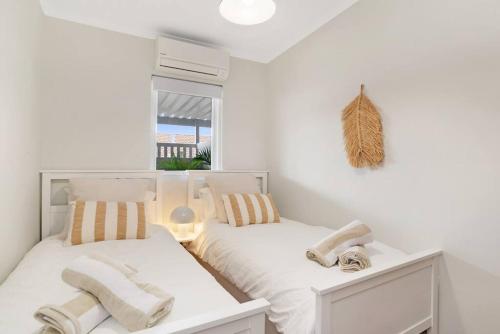 a white bedroom with two beds and a window at The Elements l Air l 4 Stunning Apartments each with Private Outdoor Dining l Walk to the Beach l Pet Family and Event Friendly l Wifi l Netflix l Outdoor Shower l Communal BBQ Pavilion and Lawn Area l in Christies Beach