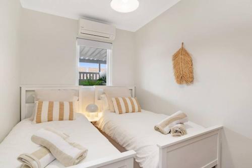 a white bedroom with two beds and a window at The Elements l Air l 4 Stunning Apartments each with Private Outdoor Dining l Walk to the Beach l Event Friendly l Wifi l Netflix l Outdoor Shower l Communal BBQ Pavilion and Lawn Area l in Christies Beach