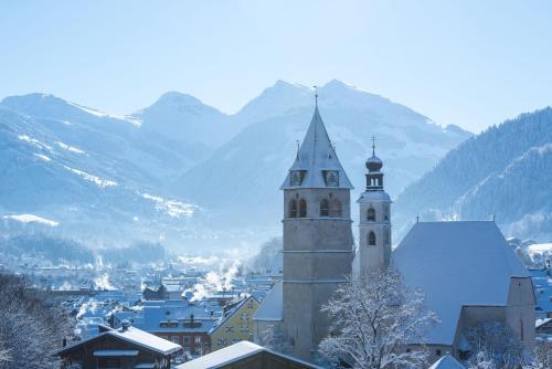 a building with a clock tower with mountains in the background at Landsitz Römerhof - Hotel Apartments in Kitzbühel