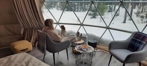 a woman sitting in a chair looking out of a window at Igloo Glamping LakeLand Camp in Imatra