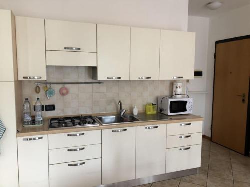 eine Küche mit weißen Schränken, einer Spüle und einer Mikrowelle in der Unterkunft Appartamento comodo per brevi periodi in Forlì