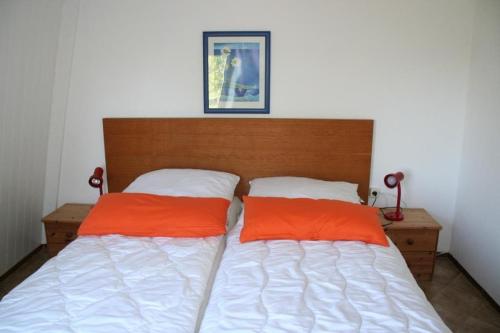 a bed with two orange pillows in a bedroom at Heggerank 36* in Nieuwvliet