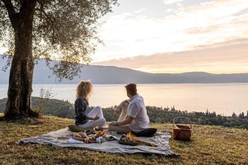 a couple sitting on a picnic blanket next to the water at Colago Private Villas Lake Garda in Toscolano Maderno